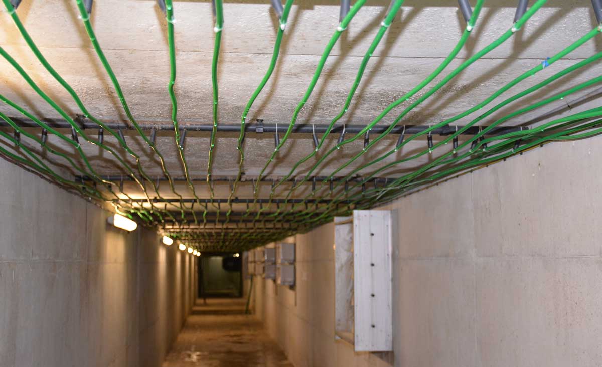 Dans la gaine centralisée. Les calories de l'air vicié sortant des salles sont récupérées par le gaz contenu dans les tuyaux verts. De fait, la température dans la gaine est basse. Ces tuyaux présentent des caractéristiques uniques de résistance à l'ammoniac, selon le concepteur. Les tuyaux restent propres en raison de l'humidité (condensation). - Illustration Un récupérateur de calories chauffe les porcelets