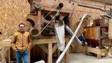 Un paysan pastier devant deux machines anciennes en bois permettant de travailler le grain.