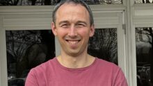 un homme souriant les bras croisés devant un bâtiment