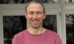 un homme souriant les bras croisés devant un bâtiment