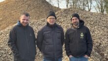 Trois hommes devant un tas de bois déchiqueté.