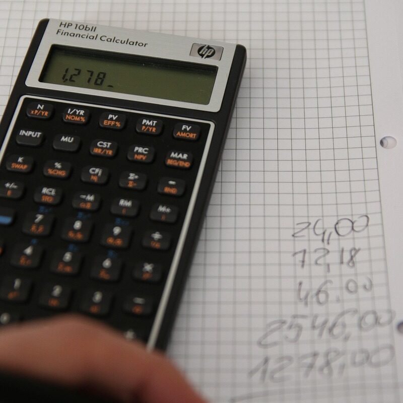 Un main, un cahier et une calculatrice. La main reporte les résultats des calculs sur le cahier - Illustration Optimiser sa CAF