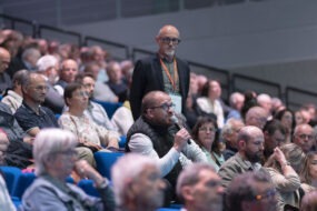 Une assemblée sur des gradins, un homme tient un micro
