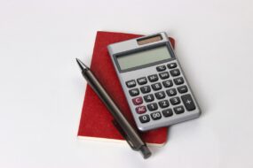 Un carnet, un crayon et une calculatrice posés sur une table blanche