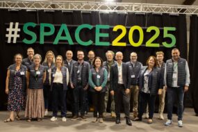 Un groupe de personnes pose devant une enseigne du Space 2025