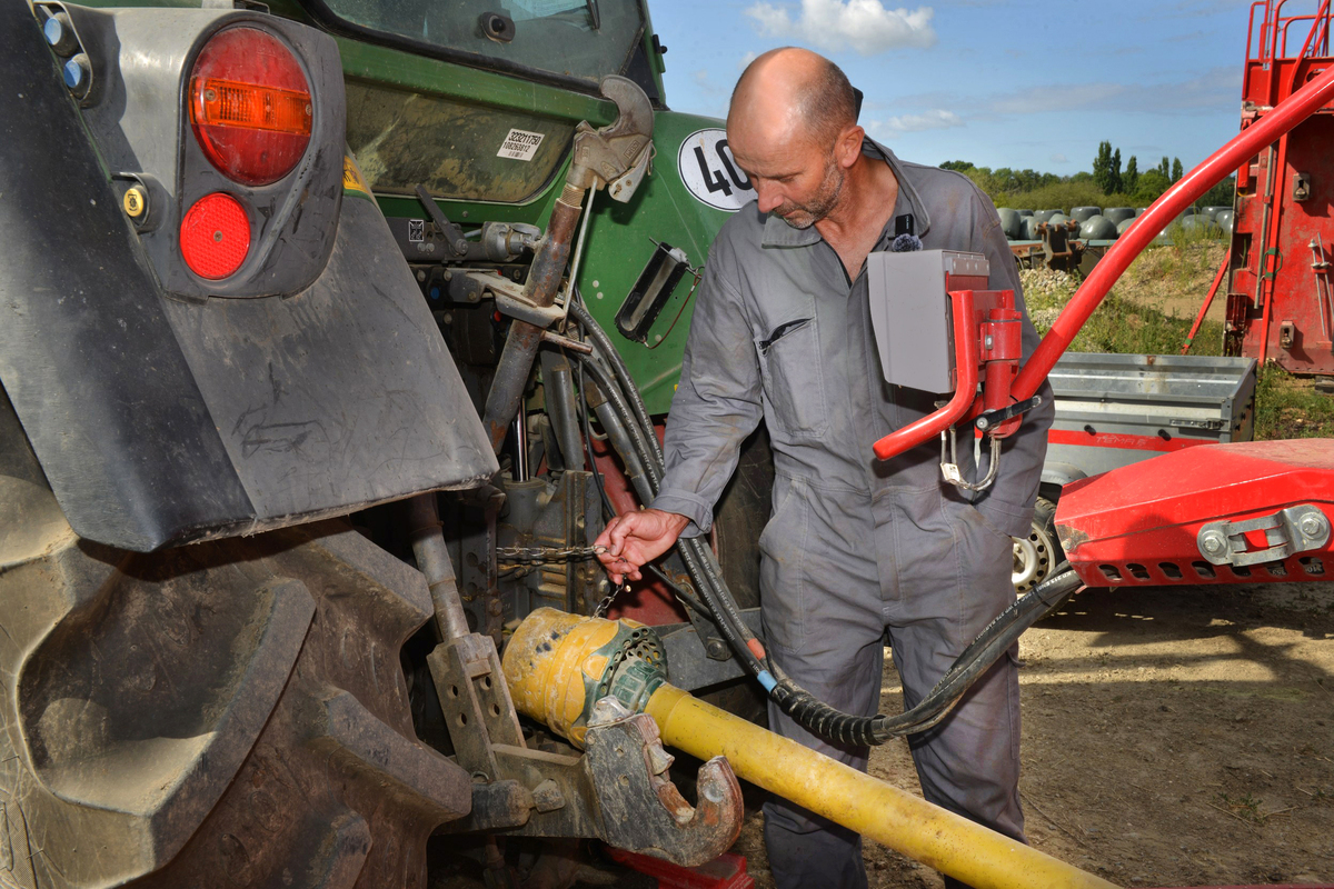 Un homme à l'arrière d'un tracteur en train d'attacher la chainette du cardan d'un outil au tracteur - Illustration groupama