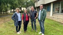 Deux hommes et deux femmes posent devant un bâtiment sur une pelouse