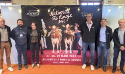 Des personnes posent devant une affiche du concours national bovin de race Pie Rouge