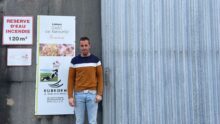 Un homme pose devant un bâtiment agricole
