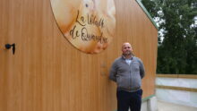 Un homme devant un bâtiment avec une enseigne d'élevage de volailles