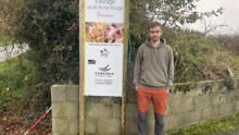 Un homme pose devant la pancarte de son élevage de porc