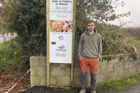 Un homme pose devant la pancarte de son élevage de porc