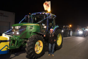 Un jeune agriculteur avec un bonnet de Noël devant un tracteur vert de marque John Deere