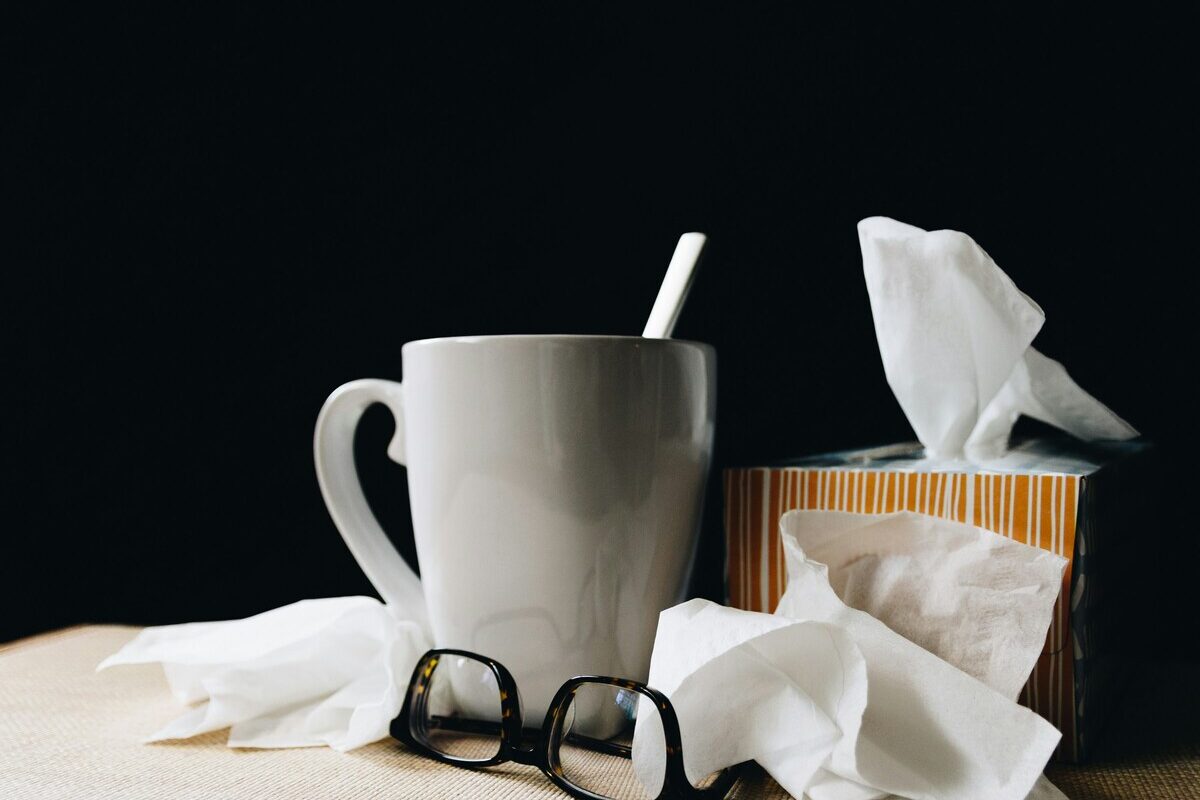 Un mug avec une cuillère, une paire de lunettes et des mouchoirs en papier sur une table - Illustration Arrêt maladie pendant les congés payés : Un changement majeur à connaître