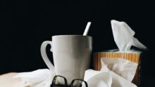 Un mug avec une cuillère, une paire de lunettes et des mouchoirs en papier sur une table
