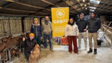 Trois femmes, trois hommes et un chien dans un bâtiment d'élevage de chèvres