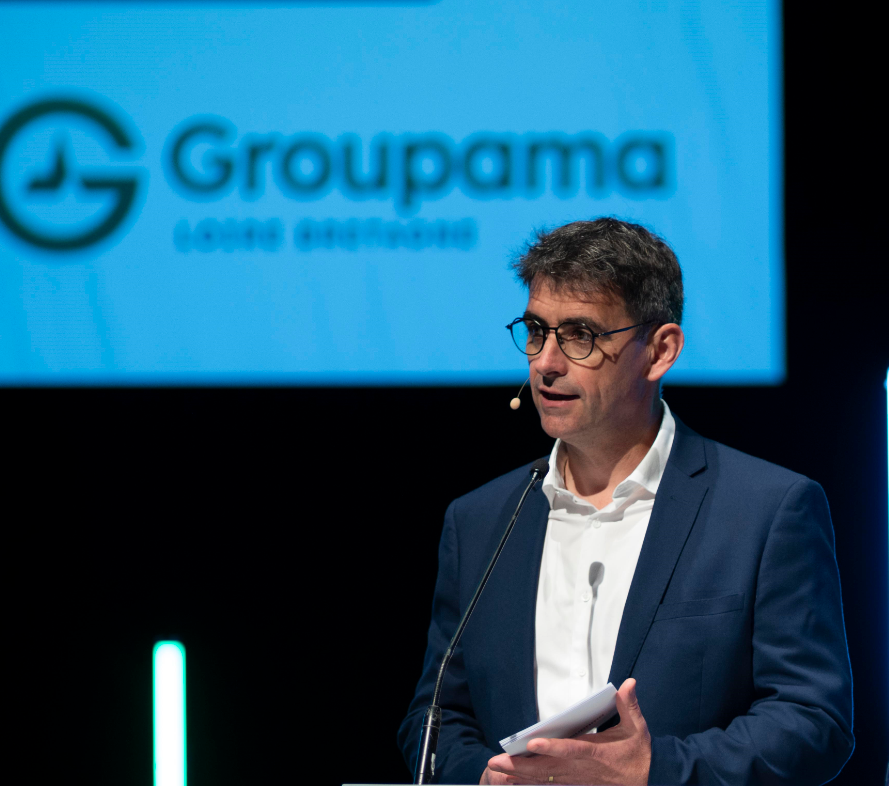 Un homme avec un micro casque à une tribune un écran projette le logo groupama derrière - Illustration Proches sur le terrain, engagés pour l’avenir