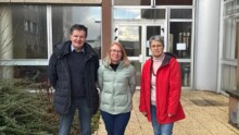 Un homme et deux femmes devant un bâtiment institutionnel