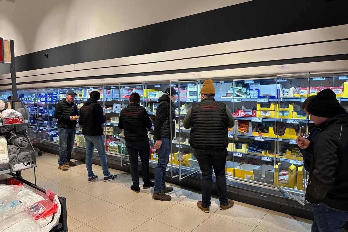 Des hommes habillés en sombre devant les rayons réfrigérés d'un supermarché - Illustration Les GMS mises sous pression