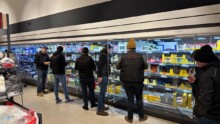 Des hommes habillés en sombre devant les rayons réfrigérés d'un supermarché