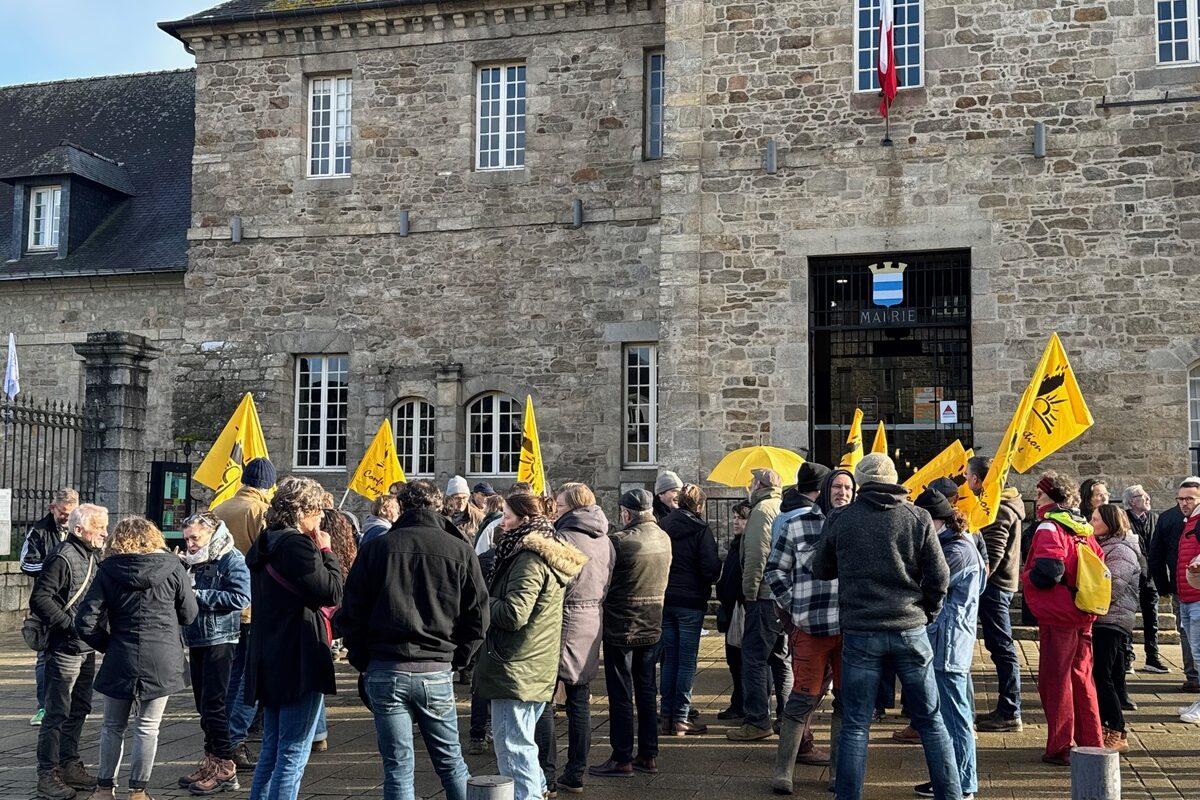 Des manifestants du syndicat agricole de la Confédération Paysanne portent leurs drapeaux jaunes devant le mur en pierres d'une mairie - Illustration Pour la Conf&rsquo;, pas de drapeau syndical sur une mairie