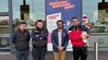 Quatre homme devant un magasin Ecomiam dont l'un porte un enfant en bas âge avec un bonnet.