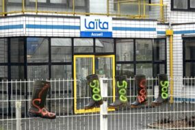 Des bottes en caoutchouc avec l'inscription 500 accrochées sur les grilles devant le bâtiment de l'entreprise laitière Laïta