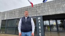 Un homme devant une mairie présentant les drapeaux de la France et de l'Europe.