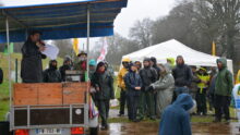 Des manifestants écoutent, sous la pluie, une personne avec un micro installée sur une remorque couverte