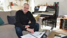 Un homme dans un camapé en train de travailler sur une table basse avec un piano derrière