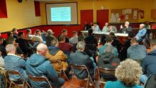 Une réunion rassemblant des gens face à des personnes assises derrière une table