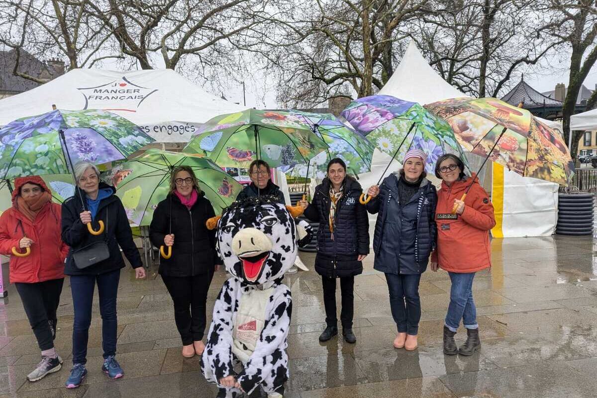 Sept femmes avec des parapluies prennent la pose avec mascotte,une vacche noire et blanche - Illustration L’association Agris56 au Vann’Ecotour