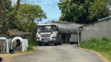 Un camion-citerne entre dans la cour d'une ferme où on aperçoit des niches à veau pour collecter la production.