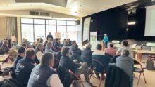 Un groupe de personne dans une salle dont une qui parle à la tribune