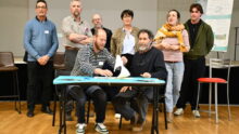 deux hommes assis signent un contrat avec des gens debout derrière
