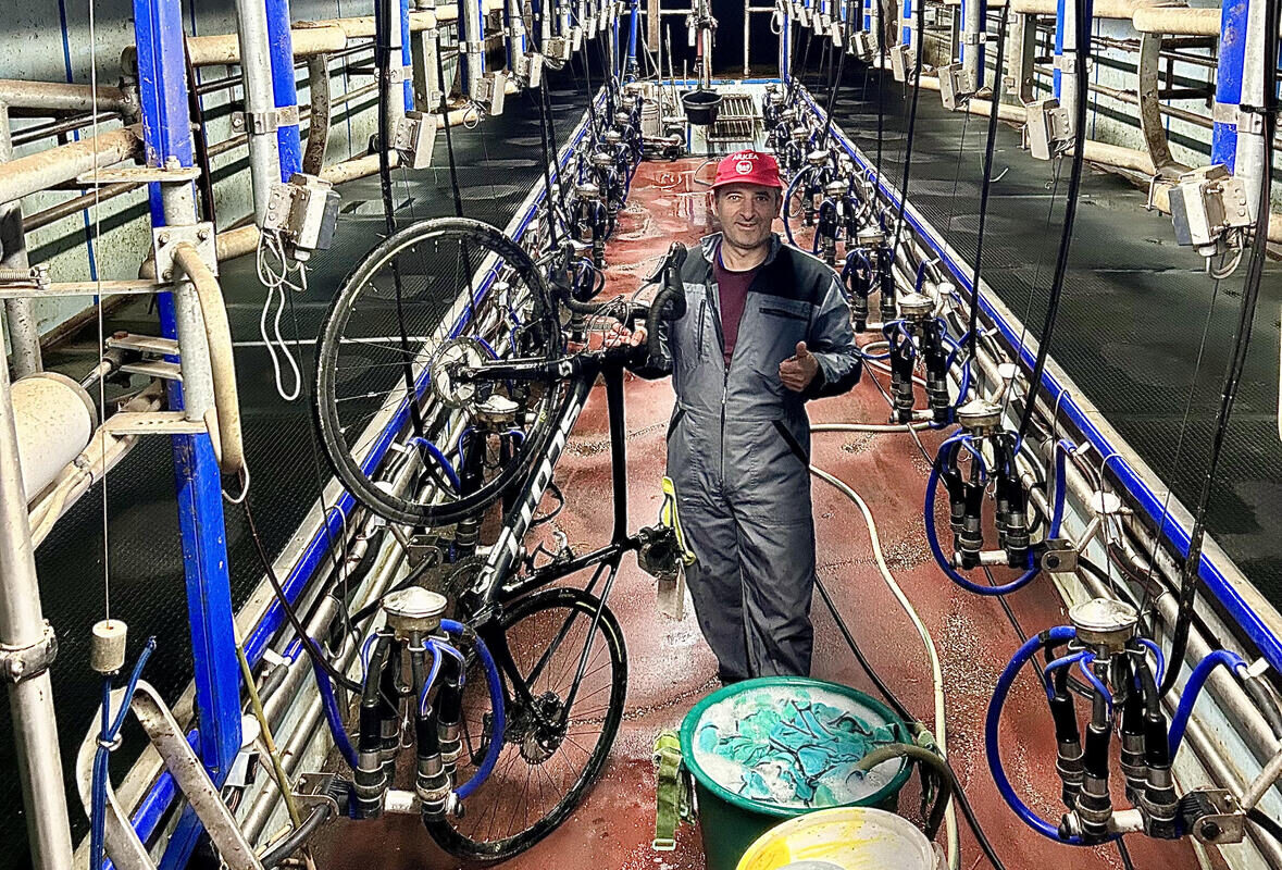 Un homme avec un vélo dans le couloir central d'une salle de traite vide - Illustration Moins de boulot, plus de vélo