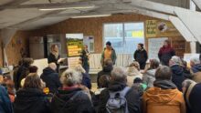 Une assemblée de personnes assises de dos face à cinq interlocuteurs debout