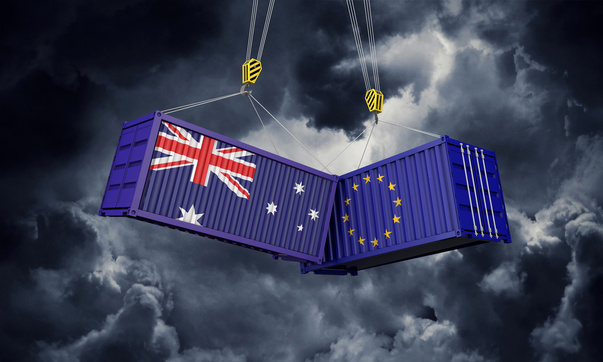 Infographie de 2 containers, un avec le drapeau australien et l'autre avec le drapeau européen. Ils sont suspendus et se cognent dans un ciel d'orage - Illustration UE/Australie : l’accord commercial reçoit un accueil mitigé 