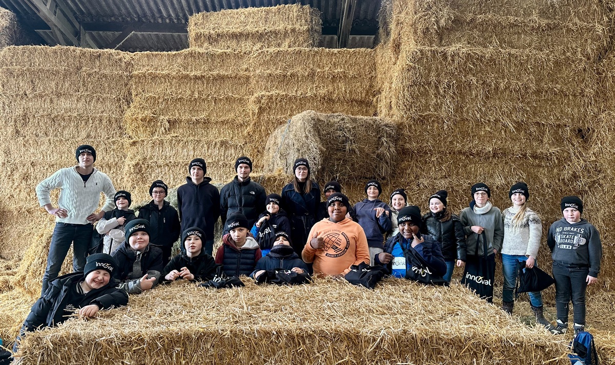 Un homme et des enfants portant des bonnets noirs devant un mur de bottes de paille dans un élevage - Illustration Les primaires à la ferme à Gurunhuel
