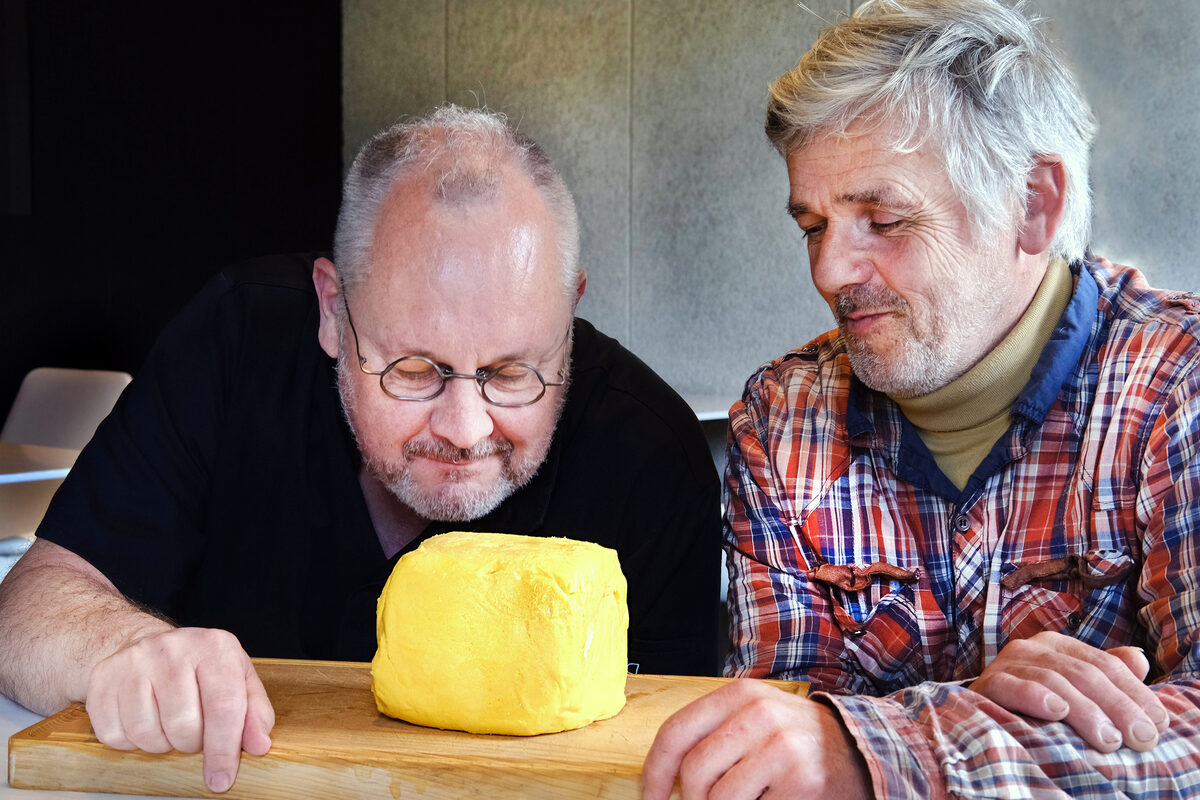 Deux hommes observent et sentent une motte de beurre artisanale posée sur une planche - Illustration L’éleveur, la Froment du Léon… et le chef étoilé