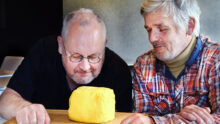 Deux hommes observent et sentent une motte de beurre artisanale posée sur une planche