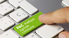 UGros plan sur un clavier d'ordinateur avec un doigt qui appuie sur la touche entrée sur laquelle il y a écrit "PAC Politique Agricole Commune"