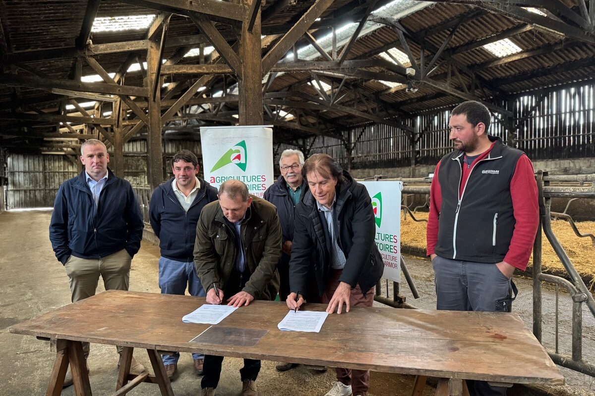 Six hommes dont deux en train de signer des documents sur une table posée dans un bâtiment agricole - Illustration Aide renouvelée du Département
