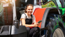 Une jeune femme souriante avec un portable à la main sur le marchepied d'un tracteur
