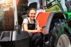 Une jeune femme souriante avec un portable à la main sur le marchepied d'un tracteur