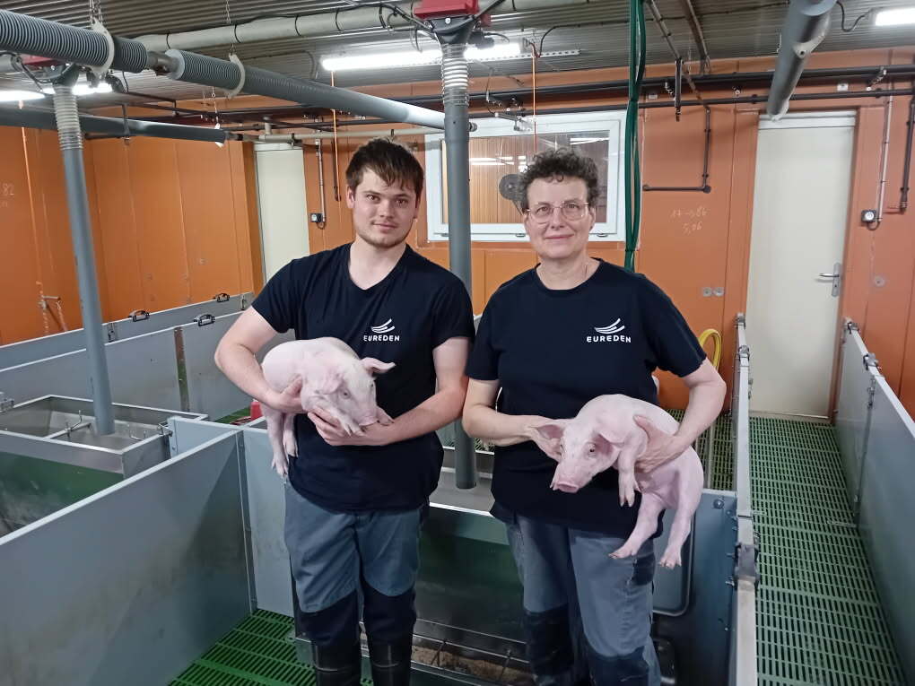 Deux éleveurs avec des porcelets dans les bras dans une salle post sevrage d'une porcherie - Illustration Eureden : une révolution nutritionnelle pour sécuriser le sevrage