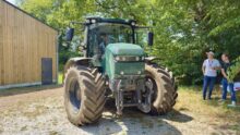 Un tracteur électrique dans une cour avec 2 hommes à l'ombre d'un arbre qui le regarde