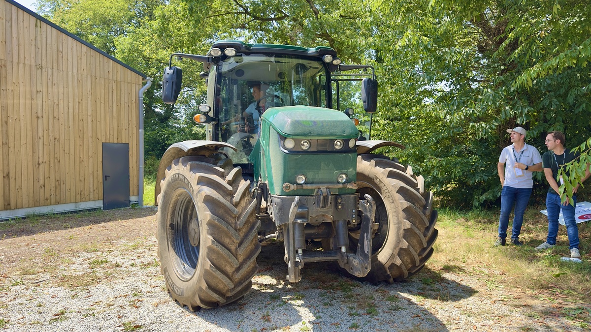 Un tracteur électrique dans une cour avec 2 hommes à l'ombre d'un arbre qui le regarde - Illustration Le plan d’électrification se renforce