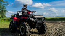 Une personne équipée (casque, gants, veste..) sur un quad dans un champ