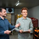 Deux hommes souriants discutent dans une chambre froide remplie de légumes